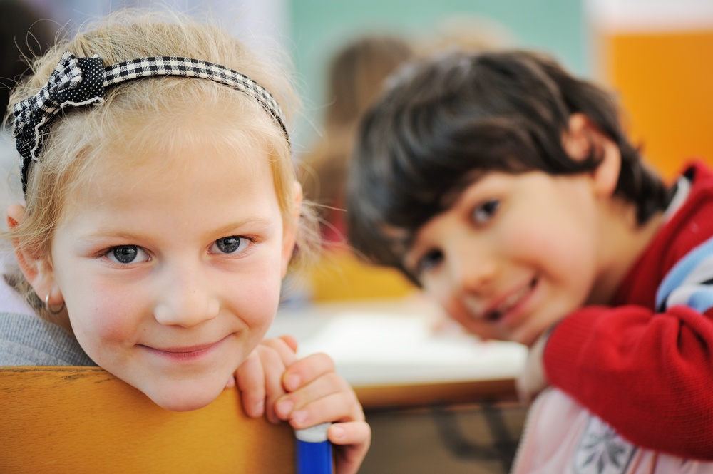 Image of smart schoolboy and schoolgirl sitting at desk and drawing while looking at camera during lesson