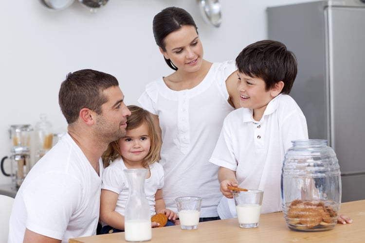 Parents and children eating biscuits and drinking milk in the kitchen